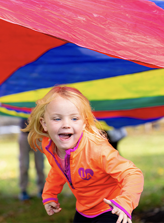 Child running under a colorful parachute outdoors