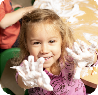 Child smiling with hands covered in foam