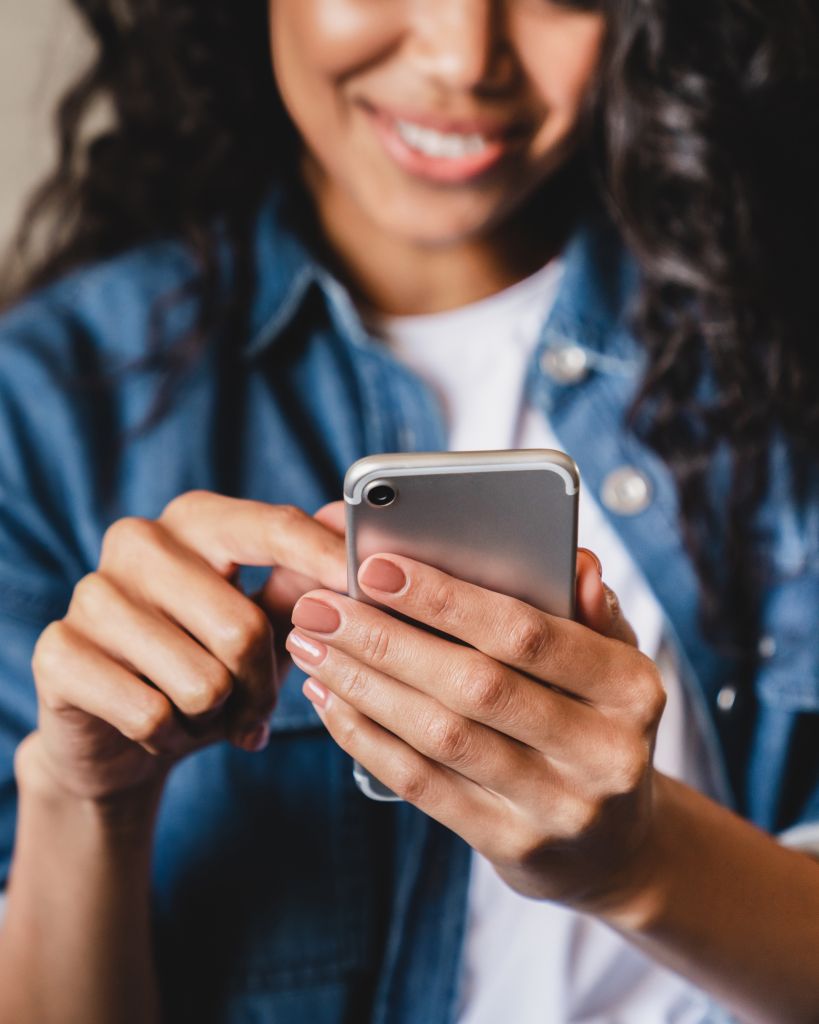 A smiling woman in a denim jacket uses a smartphone