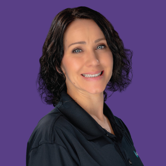 A Lifespan Childcare staff member with short dark curly hair wearing a dark uniform, smiling against a purple background