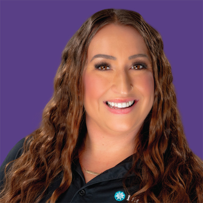 A Lifespan Childcare staff member with long wavy brown hair smiling warmly, wearing a dark uniform against a purple background